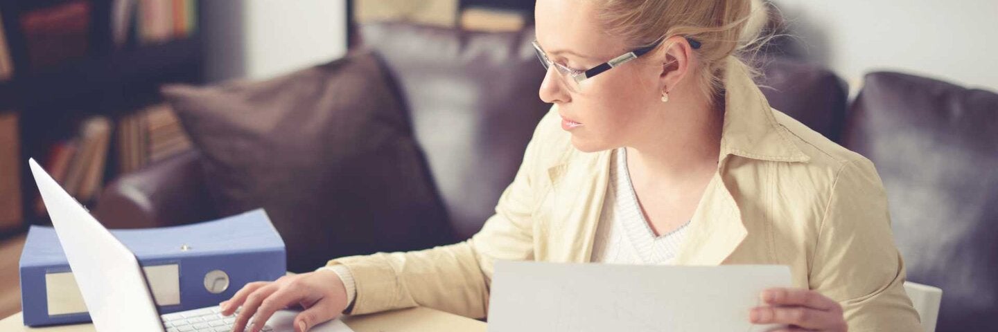 Woman sitting at the table and working on laptop with papers.