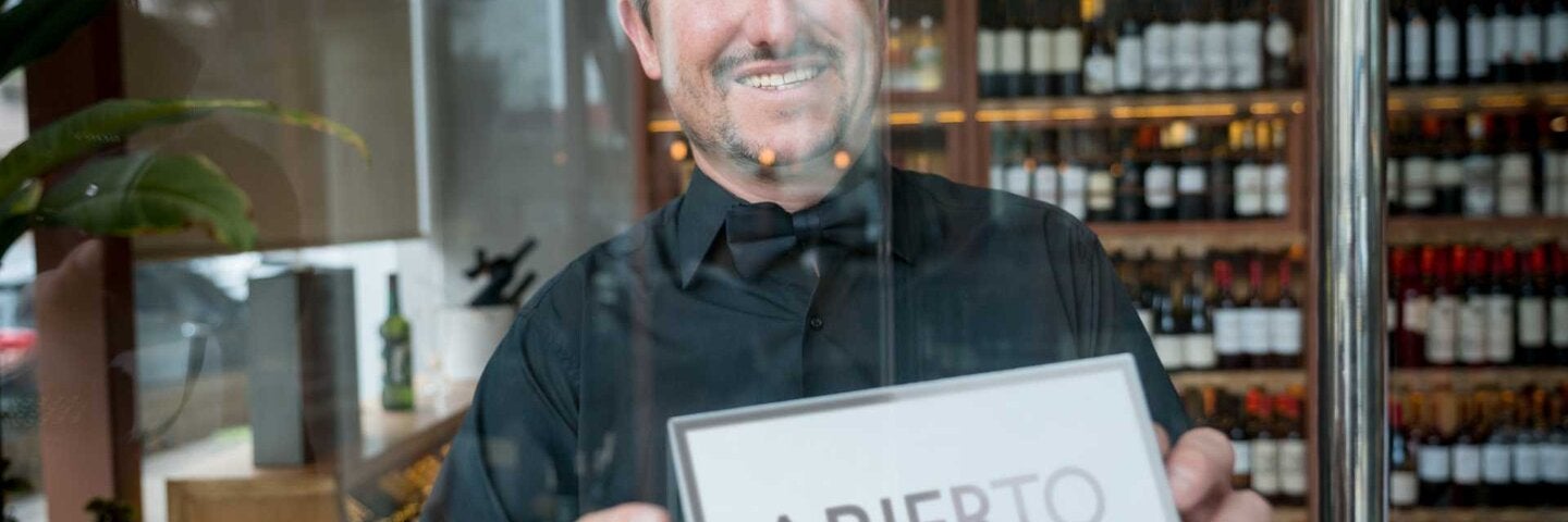 Business owner of a spanish wine store hanging an open sign on the door