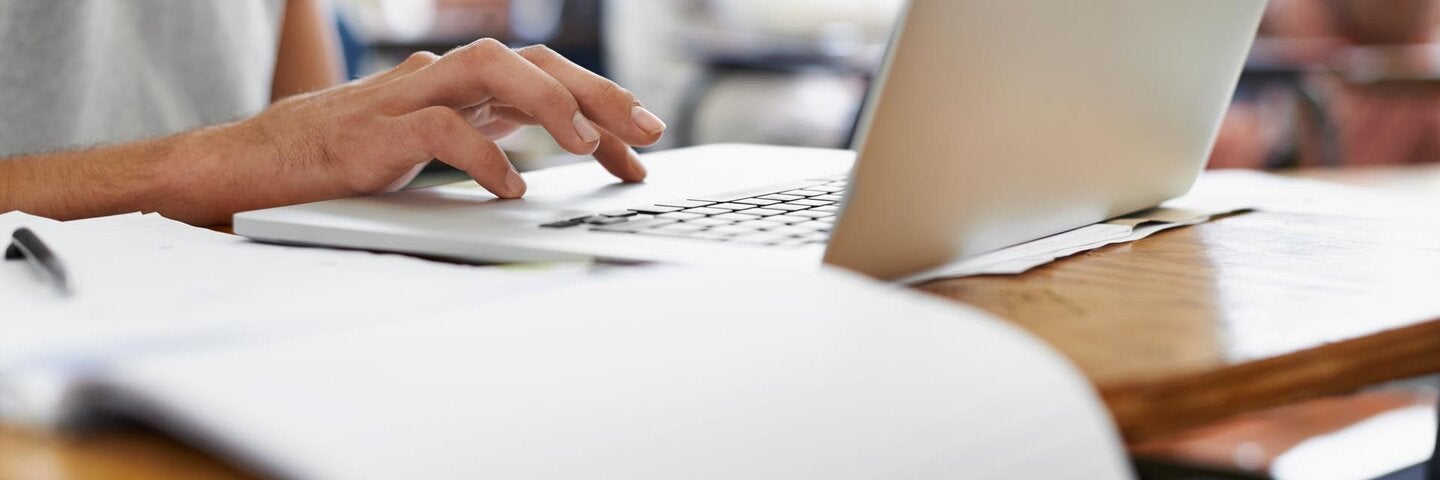 hand typing on a laptop with papers on a desk