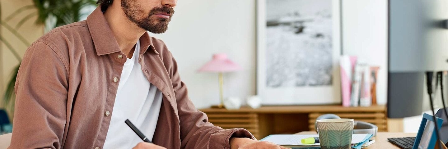 Male Entrepreneur Writing In Book At Home Office