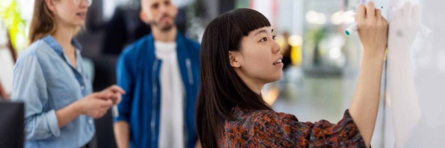 professional writing on a white board with two coworkers in the backgroun