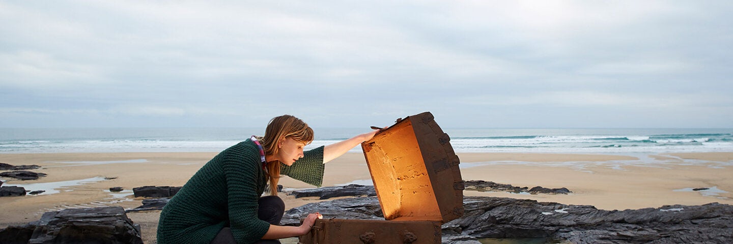 Woman opening a glowing treasure chest on an abandoned beach