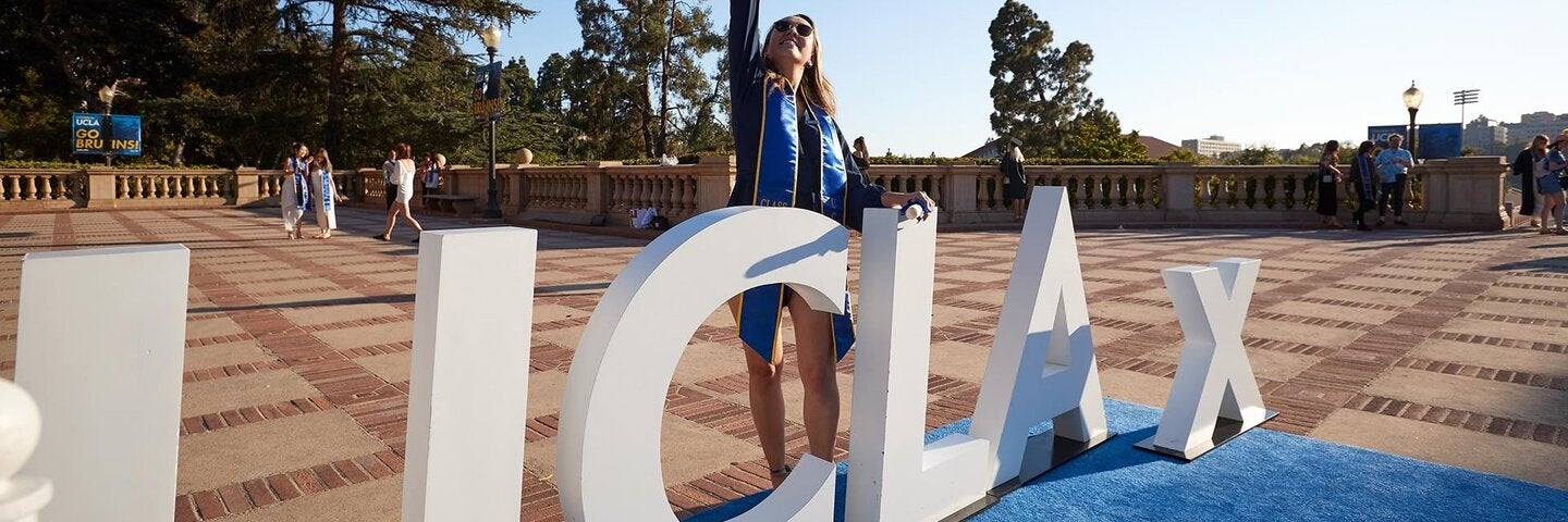 A UCLA Extension graduate jumping in front of the UCLA Extension sign.”