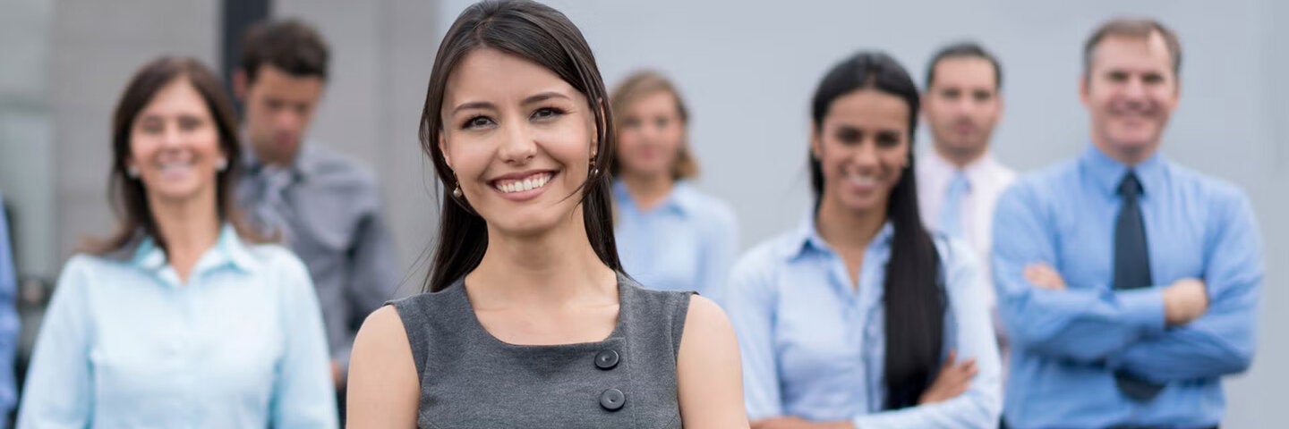 A smiling professional woman in the foreground with team members standing behind her.