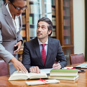 two business professionals in suits referring to an open law book
