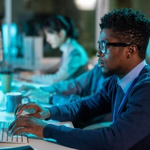 person-in-front-of computer-with-another-person-in-background-on-computer